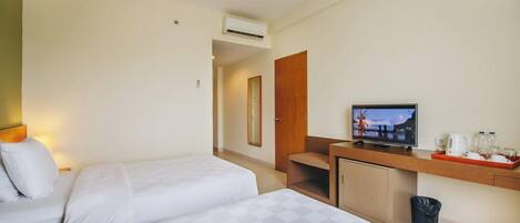 Habitación de hotel con dos camas, un escritorio con televisor, una kitchenette pequeña y un cubo de basura.