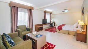 Una camera d'albergo con divano, tavolino, televisore, letto e scrivania.