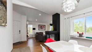 A modern living room with a fireplace, a dining area with a white table and chairs, and a view of greenery outside. - ★Modern Ritz Pointe Beach Escape★ STR 23-0009 (Dana Point)