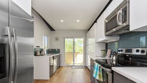 A modern kitchen with stainless steel appliances, a wooden floor, and a sliding glass door leading to a deck. - ★Modern Ritz Pointe Beach Escape★ STR 23-0009 (Dana Point)