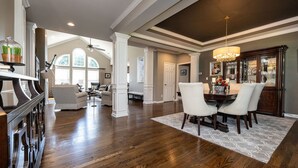 A spacious living room with a high ceiling, a dining area with a chandelier, and a view of the outdoors through large windows. - Beautiful 4 BR, 4.5 Bath, Executive Home w In Ground Pool & Handicap Accessible! (Louisville)