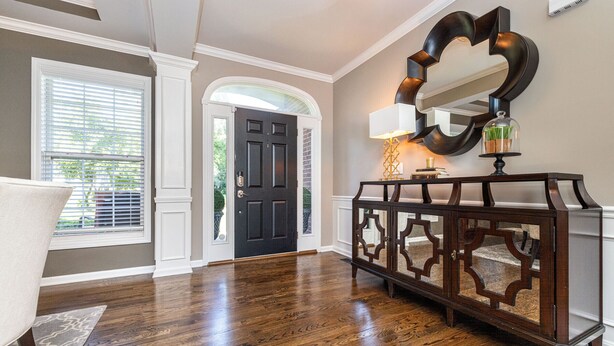 A hallway with hardwood flooring, a dark wooden door, a white armchair, and a console table with a mirror and lamp. - Beautiful 4 BR, 4.5 Bath, Executive Home w In Ground Pool & Handicap Accessible! (Louisville)