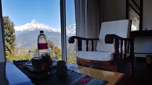 A room with a view of snow-capped mountains, a wooden chair, a table with a bottle, a glass, and a cup. - ES Deurali Resort. (Pokhara)