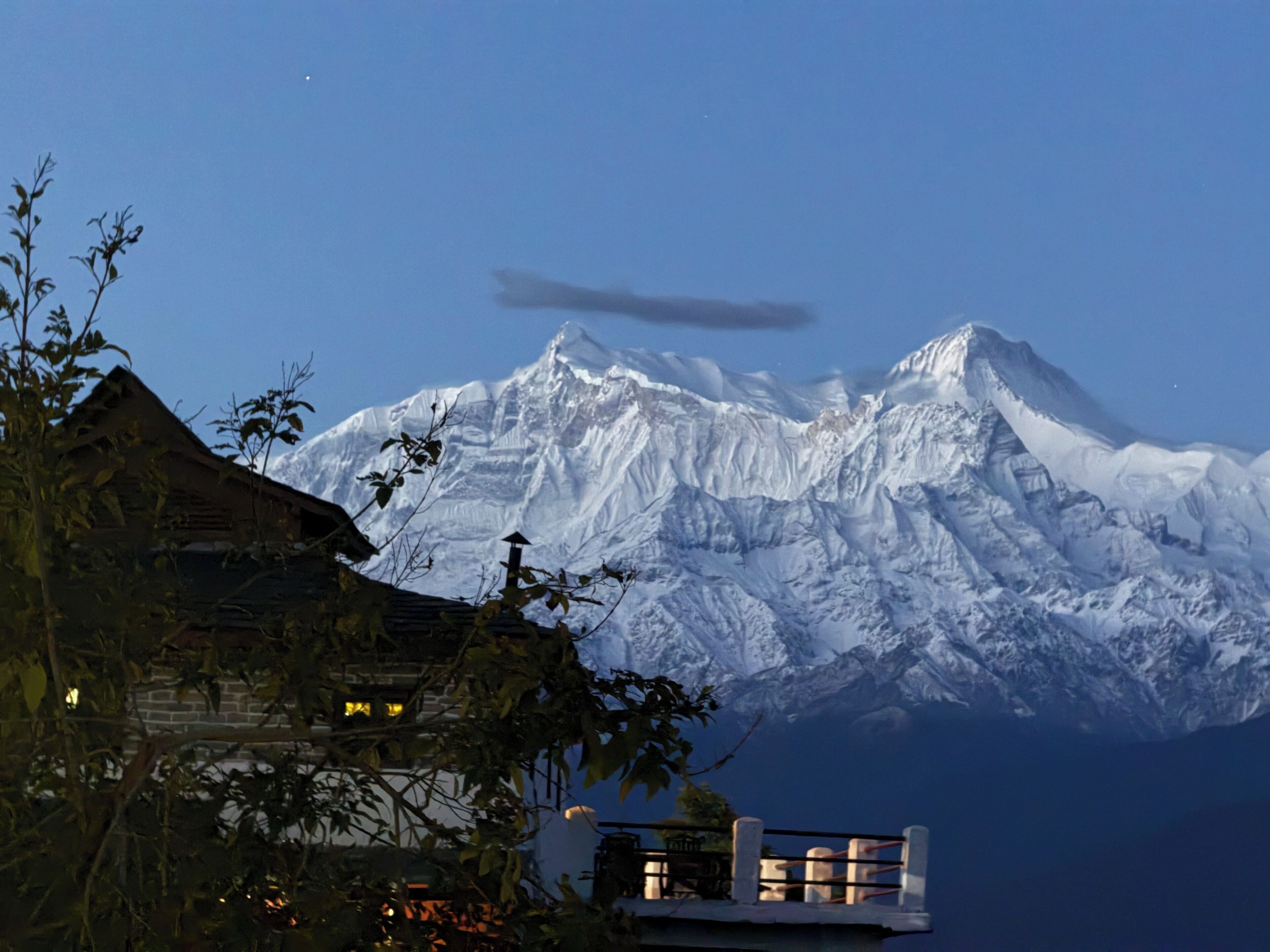 Una montagna con cime innevate, un edificio in legno con tetto spiovente e un piccolo balcone con ringhiere.