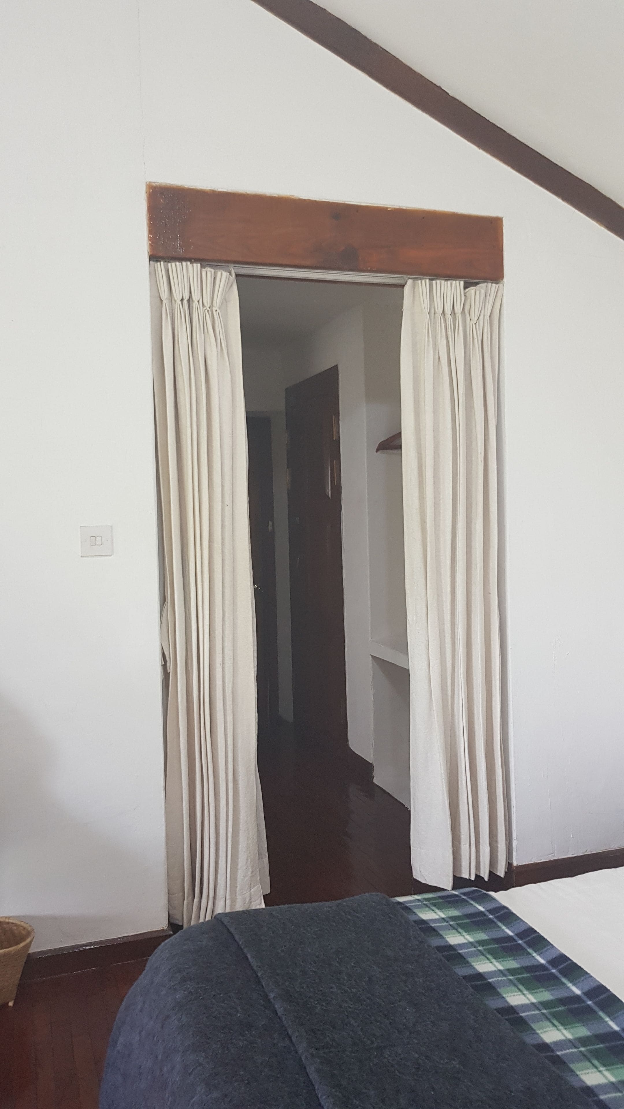 Ein Zimmer mit einem Bett, Holzboden und einer Tür mit Vorhängen.