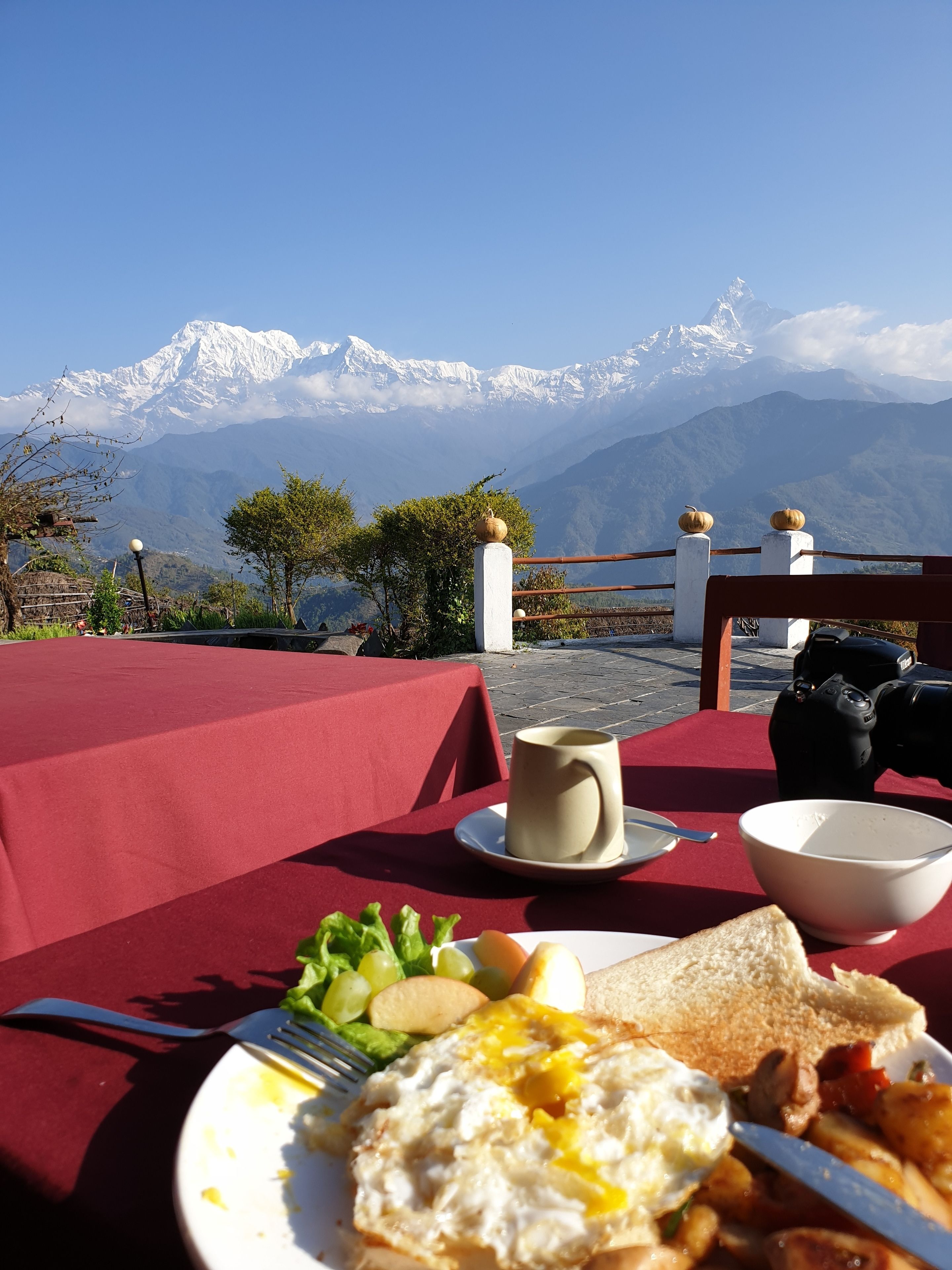 A table with breakfast items and a camera, overlooking a mountain range.