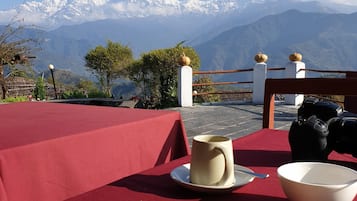 A table with breakfast items and a camera, overlooking a mountain range.