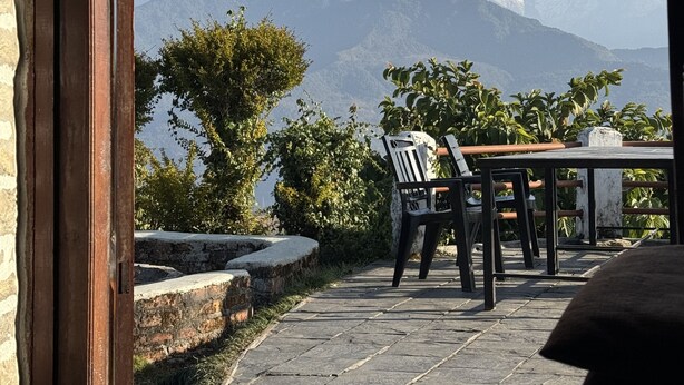 A patio with a table and chairs, overlooking a mountain range with snow-capped peaks. - ES Deurali Resort. (Pokhara)