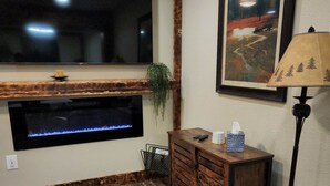 A living room with a fireplace, a mounted TV, a painting, and a lamp. - Experience Unparalleled Luxury and Convenience at Our Exquisite Condo (West Yellowstone)
