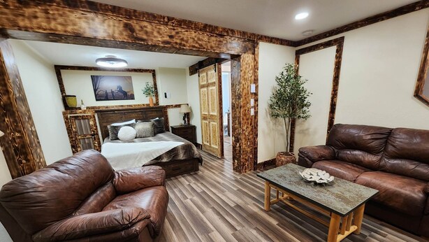 A cozy living room with a wooden floor, leather sofas, a coffee table, and a bed with a wooden headboard. - Experience Unparalleled Luxury and Convenience at Our Exquisite Condo (West Yellowstone)