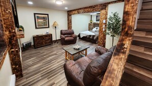 A spacious living room with a brown leather sofa, a wooden coffee table, and a wooden floor. There is a lamp, a framed picture on the wall, and a bed in the background. - Experience Unparalleled Luxury and Convenience at Our Exquisite Condo (West Yellowstone)