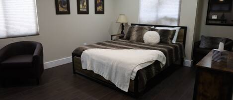 A bedroom with a large bed, a chair, a nightstand, and a dresser.