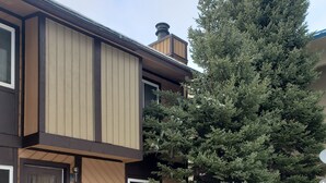 A two-story house with a wooden exterior, a chimney, and a large evergreen tree. - Experience Unparalleled Luxury and Convenience at Our Exquisite Condo (West Yellowstone)