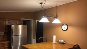 A kitchen with a stainless steel refrigerator, wooden cabinets, a wooden island with a chair, and pendant lighting. - The West Bay Lodge offers spacious amenities for a perfect getaway.  (Cedar Island)