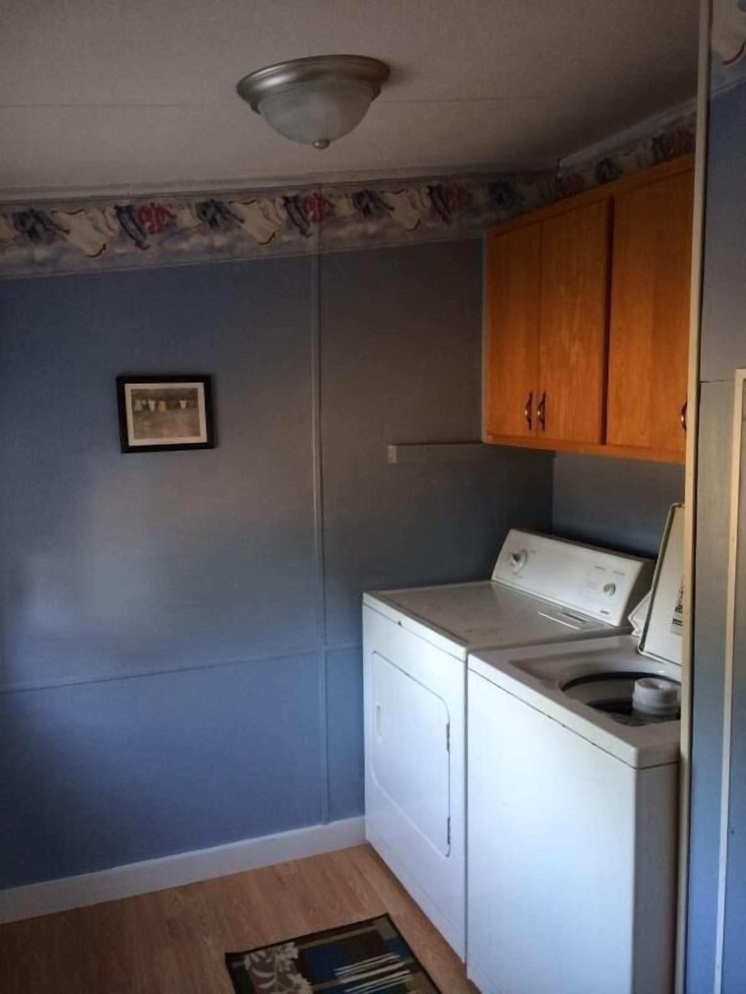 A laundry room with a washing machine and dryer, wooden cabinets, and a small framed picture on the wall.