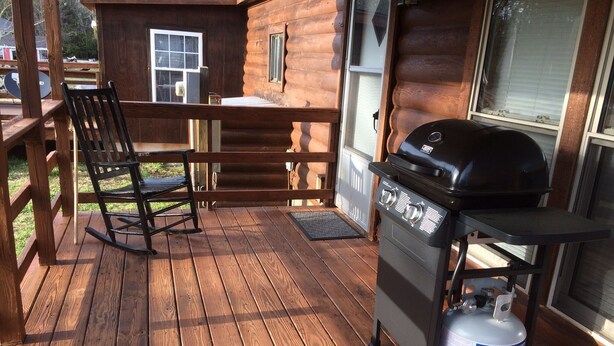 A wooden deck with a grill and propane tank, a rocking chair, and a window overlooking a yard. - The West Bay Lodge offers spacious amenities for a perfect getaway.  (Cedar Island)