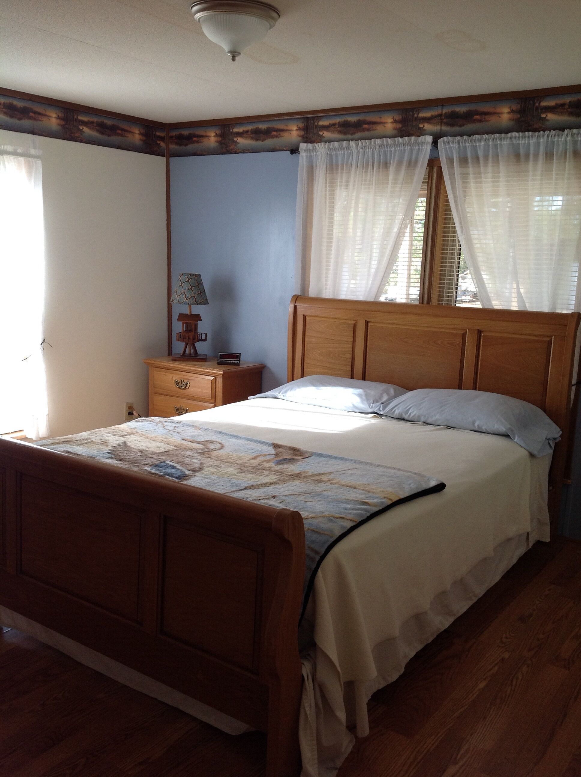 A bedroom with a wooden bed, a nightstand with a lamp, and a wall with a painted landscape.