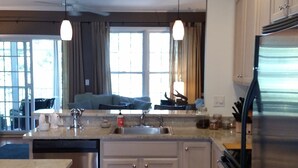 A modern kitchen with wooden cabinets, a stainless steel refrigerator, and pendant lighting. - Gated Community: Top Corner Unit, Screened Porch Facing Woods, Beautiful Pool (Rehoboth Beach)