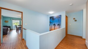 A hallway with light blue walls, wooden flooring, and a painting of palm trees.