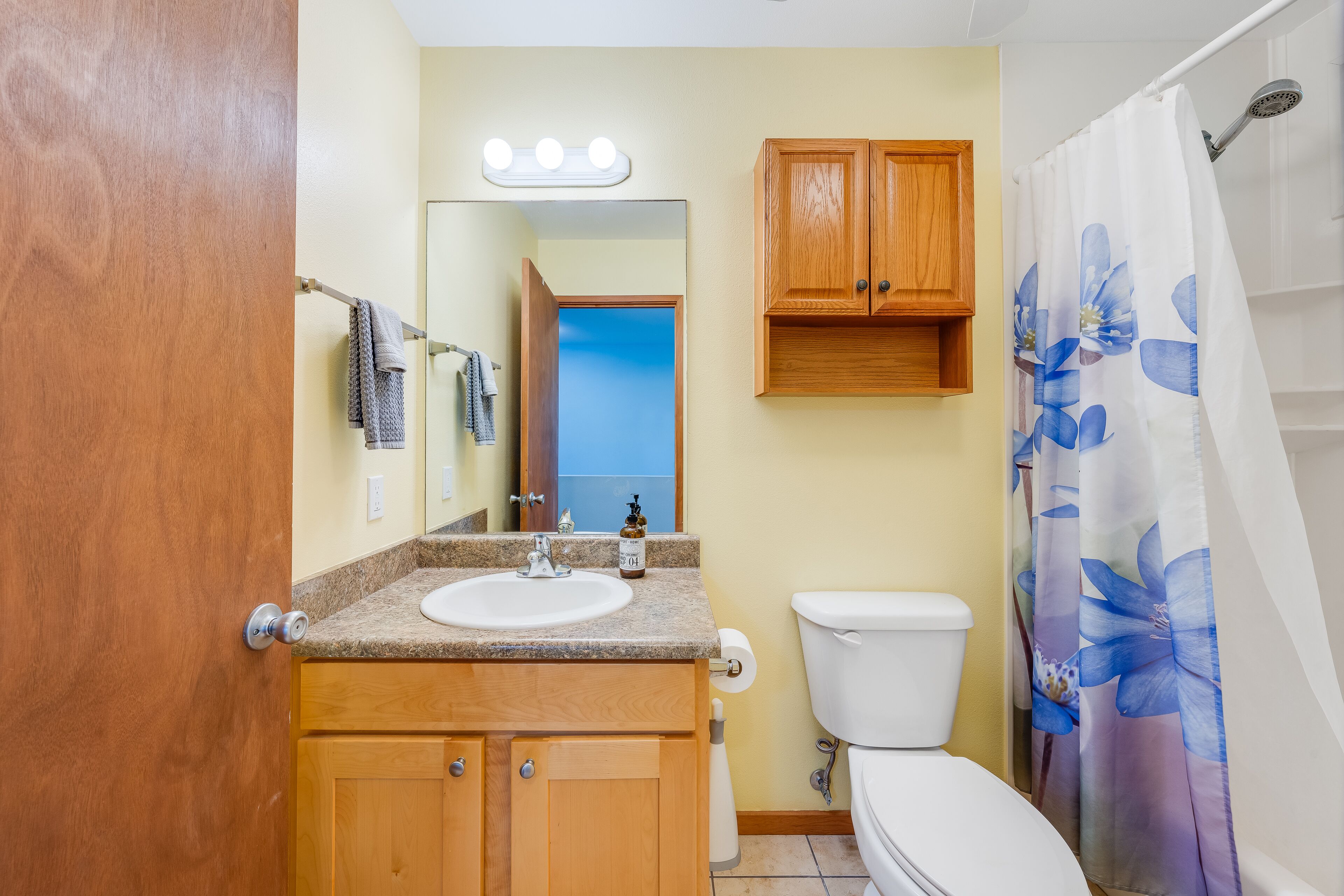A bathroom with a wooden vanity, a sink, a toilet, and a shower curtain with a floral pattern.