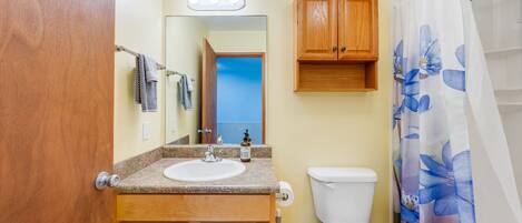A bathroom with a wooden vanity, a sink, a toilet, and a shower curtain with a floral pattern.