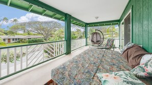 A balcony with a bed, a hanging chair, and a view of a residential area.