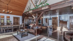 A spacious living area with a large wooden dining table, leather sofas, and a kitchen in the background.