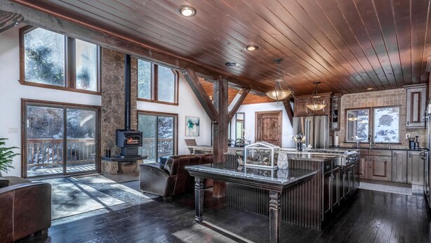 A spacious kitchen with a large island, wooden beams, and a stone fireplace.