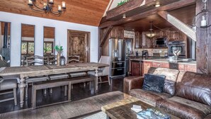A spacious living area with a wooden dining table, a leather sofa, and a kitchen with modern appliances.