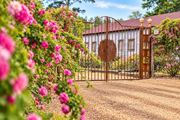 Une entrée fermée par un portail en métal rustique, une clôture en bois et, au fond, un bâtiment avec un toit rouge.