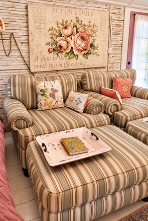 Un canapé à rayures agrémenté d’un coussin décoratif, un plateau avec un carnet, et un mur orné d’un motif floral et d’un texte.