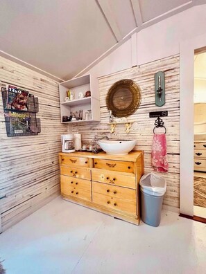 A bathroom with a wooden vanity, a white sink, and a trash bin.
