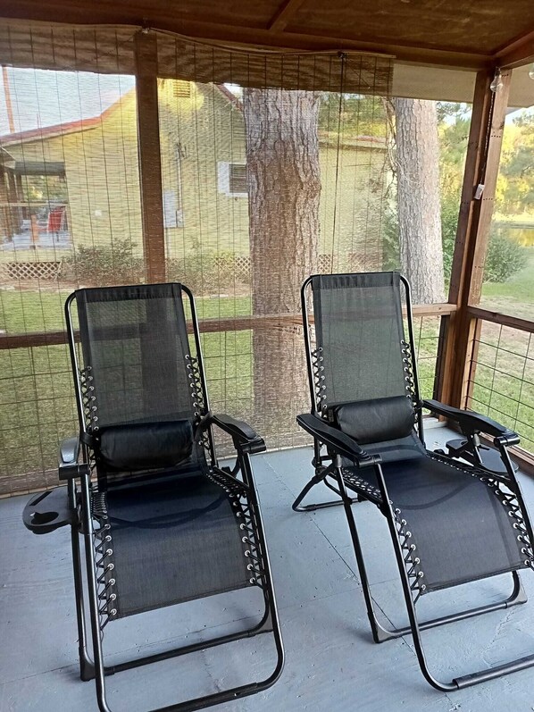 Deux fauteuils de relaxation noirs à structure métallique et dotés de roulettes, placés sur un sol en béton dans un espace abrité, avec vue sur une cour et des arbres.