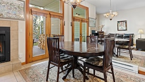 Un espace repas comprenant une grande table en bois, six chaises rembourrées, un lustre et une cheminée.