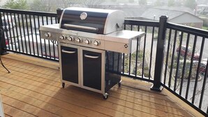 Een barbecue op een houten terras met een zwarte reling.