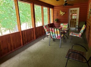 Una cabaña de madera con ventanas grandes, un ventilador de techo y una mesa de comedor con sillas coloridas.