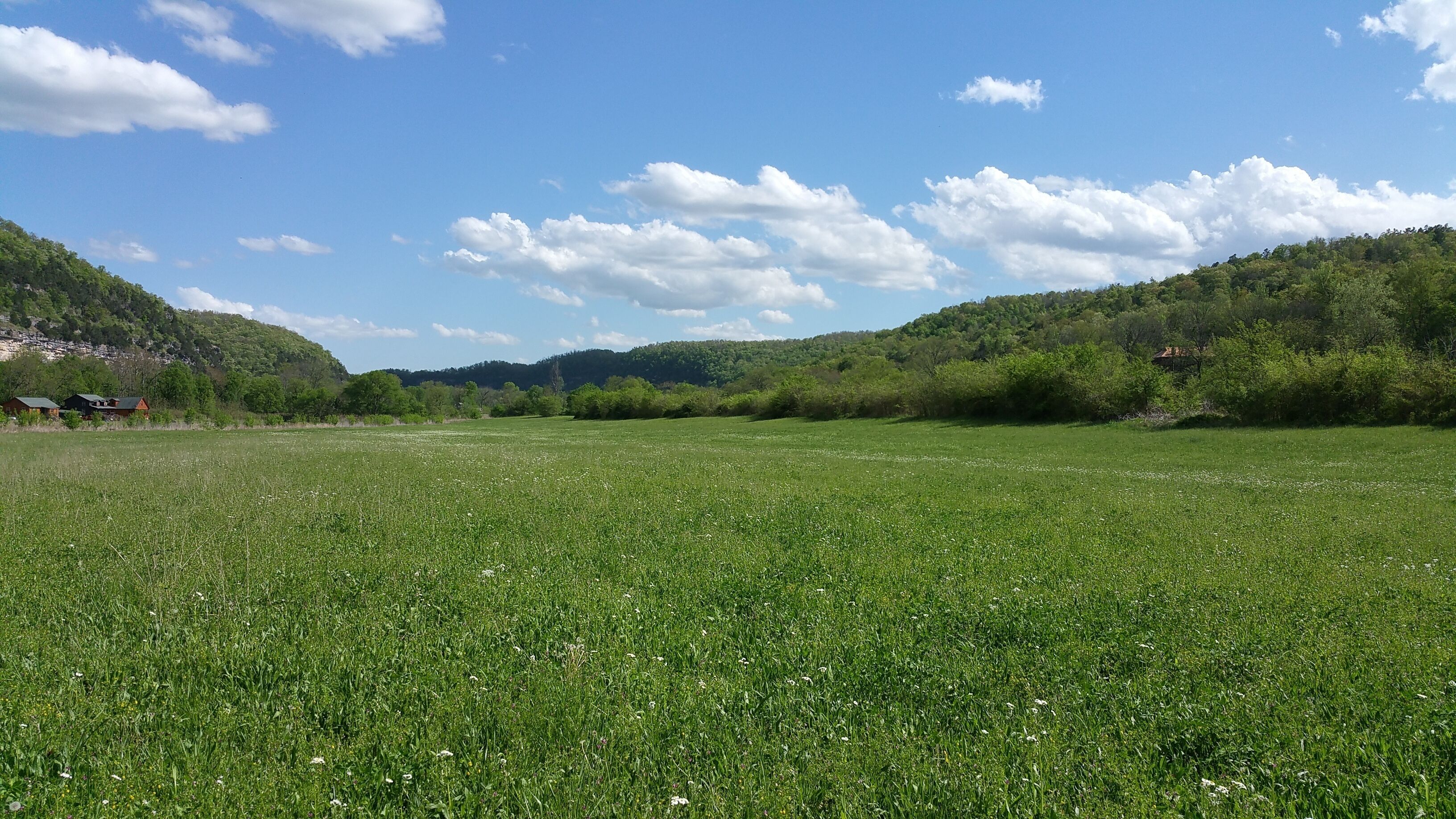 Un campo cubierto de hierba con cielo despejado y colinas a lo lejos.