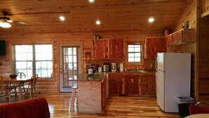 A spacious kitchen with wooden cabinets, a refrigerator, and a dining area with chairs and a table. - Beautiful cabin style home backing up on the White River! (Mountain View)