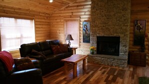 A cozy log cabin interior with a stone fireplace, a leather sofa, and wooden flooring. - Beautiful cabin style home backing up on the White River! (Mountain View)