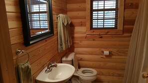 Baño de cabaña de madera con lavamanos, inodoro y dos ventanas con persianas.