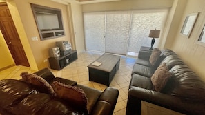 A living room with a sofa, a coffee table, a TV, and a sliding door leading to a balcony.