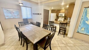 A dining area with a large wooden table and chairs, a kitchen in the background, and a map on the wall.