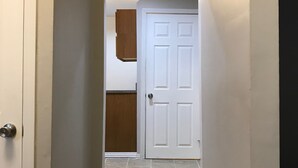 Un couloir avec une porte blanche au fond, un meuble en bois au-dessus, et un sol carrelé.