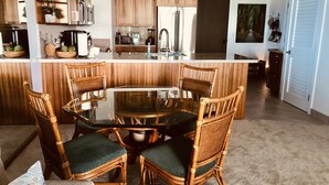 A modern kitchen with wooden cabinets, a central island, and a dining area with wicker chairs and a glass table.