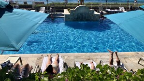 A pool area with lounge chairs and umbrellas, a view of the ocean, and a statue.