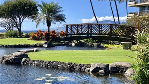 A serene garden with a pond, palm trees, and a wooden bridge.