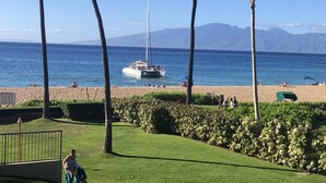 A beach with a sailboat, palm trees, and mountains in the background.