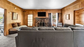 Un salon chaleureux avec une cheminée en pierre, des murs en bois et un grand canapé gris.