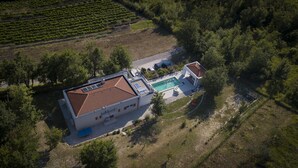 Eine Vogelperspektive eines Hauses mit Swimmingpool, umgeben von Bäumen und einem Weinberg.