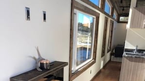 Een kamer met houten vloer, een ingebouwde bank met opbergruimte, een raam met uitzicht en een keukenhoek met een spoelbak en aanrecht.